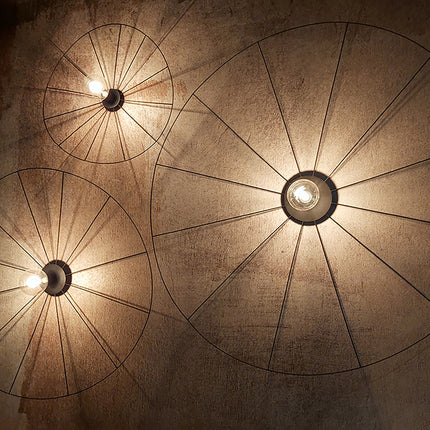 Appliques circulaires filaires noires allumées sur un mur de béton, halo de rayons chaleureux