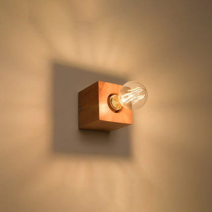 Applique cube en bois naturel allumée au mur, lumière chaude diffusée autour du cube en bois.