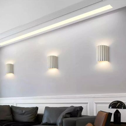 Trois appliques murales en résine cannelée blanches alignées sur un mur de salon, éclairage haut et bas chaleureux