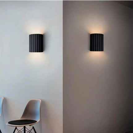 Applique murale en résine cannelée allumée sur un mur clair et un mur foncé, deux halos de lumière chaude haut et bas