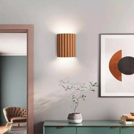 Applique murale en résine cannelée orange allumée sur un mur clair de salon, halo doux, cadre décoratif à côté