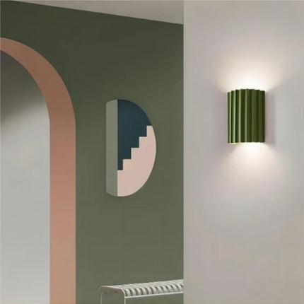 Applique murale en résine cannelée verte allumée dans une entrée au mur vert olive, à côté d'une décoration murale
