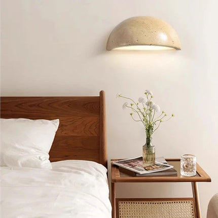 Applique murale travertin diffusant une lumiere douce dans une chambre au lit et chevet en bois