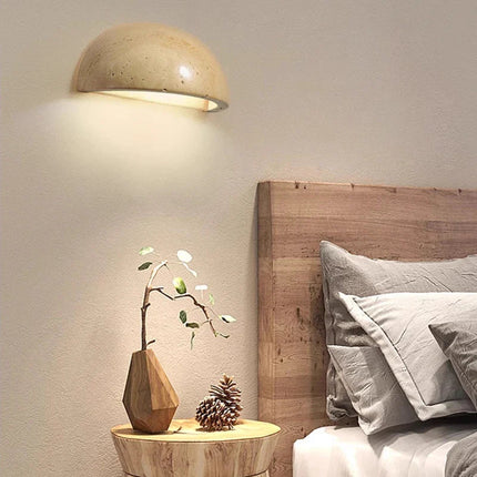 Applique en travertin allumee au-dessus d'une table de chevet en bois dans une chambre nordique