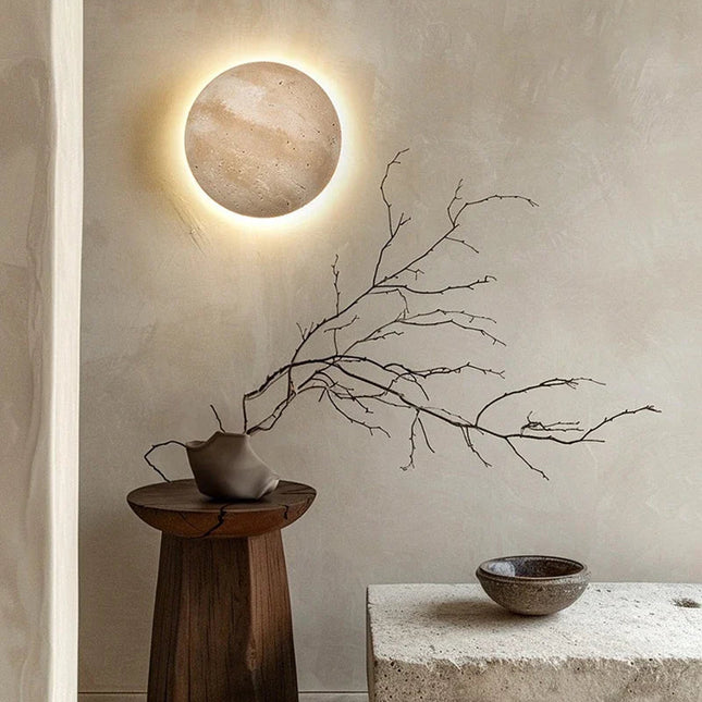 Applique murale en travertin allumée avec halo chaud dans un salon japandi et branche décorative