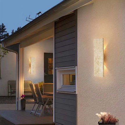 Appliques en travertin sur la façade d'une maison contemporaine diffusant une lumière chaude en soirée