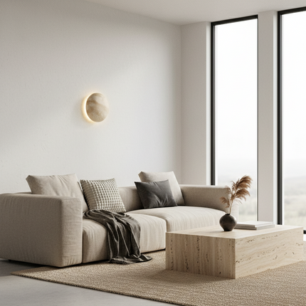 Applique ronde en travertin éclairée dans un salon minimaliste beige avec canapé et grande baie