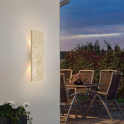Applique en travertin allumée sur un mur extérieur près d'une terrasse de jardin à la tombée du jour