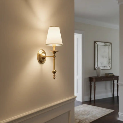 Applique murale vintage en laiton doré allumée dans une entrée cosy, lumière douce et chaleureuse