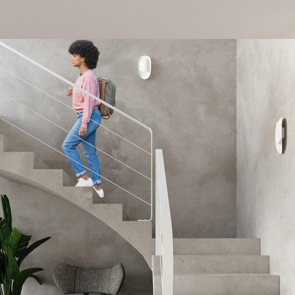 Applique Vortex blanche allumée dans une cage d'escalier, avec une personne descendant les marches