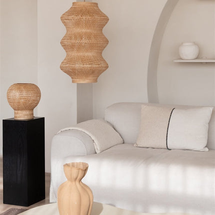 Luminaire en bambou tressé au plafond, lumière dorée diffusée dans une pièce épurée avec plante suspendue et patère en laiton.