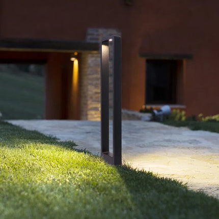 Borne LED d'extérieur anthracite allumée devant une maison en pierre au crépuscule