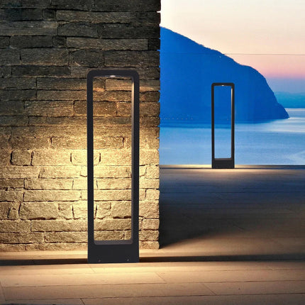 Borne d'extérieur LED anthracite éclairant un mur en pierre sur une terrasse face à la mer