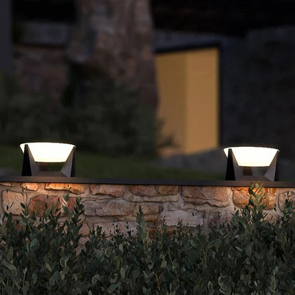 Bornes solaires blanches posées sur un muret en pierre dans un jardin le soir