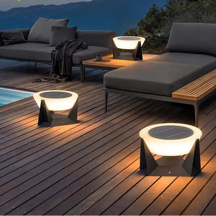 Bornes solaires noires allumées sur une terrasse en bois au bord d'une piscine à la tombée du jour