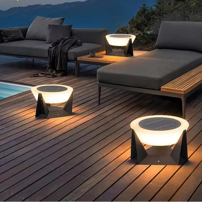 Bornes solaires noires allumées sur une terrasse en bois au bord d'une piscine à la tombée du jour