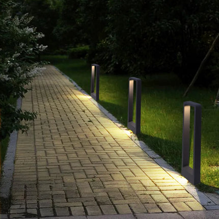 Bornes LED anthracite balisant une allée pavée bordée de végétation la nuit