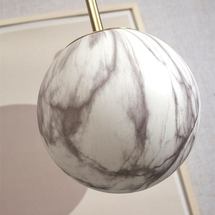 Gros plan sur le globe en verre effet marbre de la suspension Carrara et sa fixation dorée