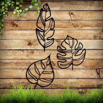 Trois feuilles tropicales en métal noir sur un mur en bois clair, ambiance nature
