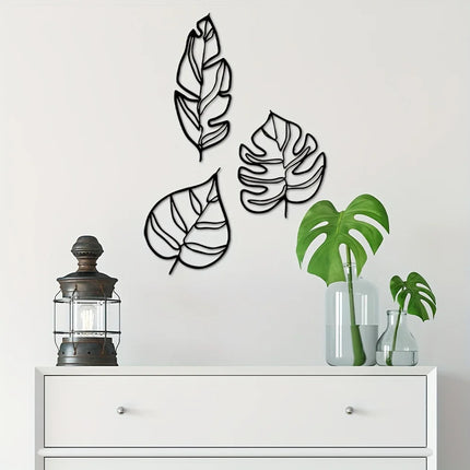 Décoration murale trois feuilles en métal noir au-dessus d'une commode blanche, avec lanterne et plante monstera