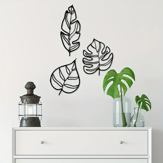 Décoration murale trois feuilles en métal noir au-dessus d'une commode blanche, avec lanterne et plante monstera