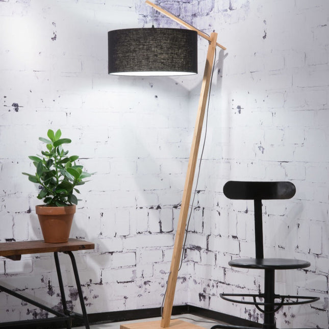 Lampadaire Andes en bambou et lin noir dans un salon, silhouette arquée près d'un plant vert
