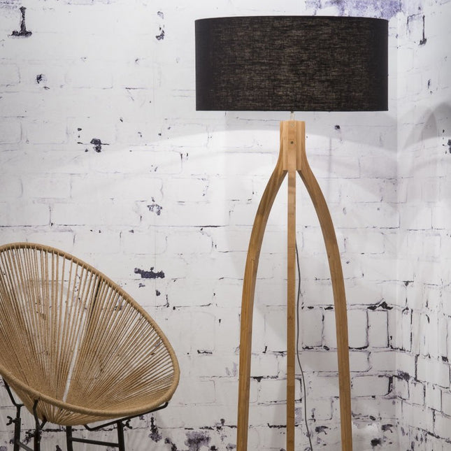 Lampadaire Annapurna en bambou tripode et abat-jour en lin noir, dans un salon avec fauteuil en corde tressée