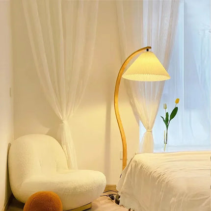 Lampadaire nordique en bois courbé dans un coin cosy blanc près d'un lit et d'un fauteuil