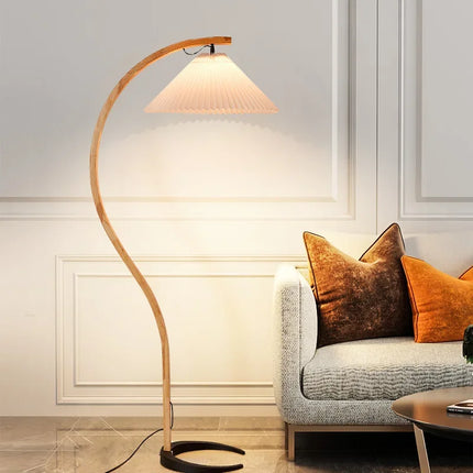 Lampadaire arqué en bois derrière un canapé gris avec coussins orange dans un salon
