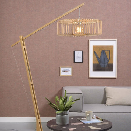 Lampadaire arqué Bromo en bambou naturel au-dessus d'un canapé gris dans un salon chaleureux