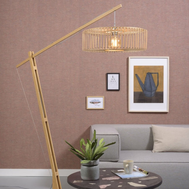 Lampadaire arqué Bromo en bambou naturel au-dessus d'un canapé gris dans un salon chaleureux