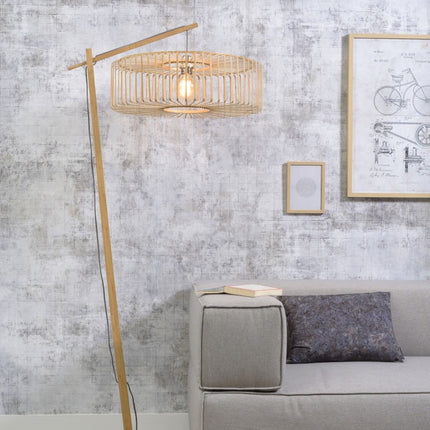 Lampadaire Bromo en bambou naturel arqué, abat-jour tressé allumé près d'un canapé gris dans un salon lumineux