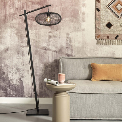 Lampadaire Cango en métal noir filaire dans un salon avec canapé gris, ambiance tamisée et jeu d'ombres graphiques