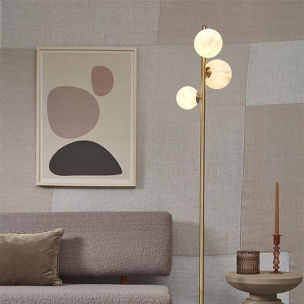 Lampadaire Carrara trois globes en verre effet marbre blanc sur tige dorée, près d'un canapé dans un salon