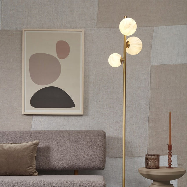 Lampadaire Carrara trois globes en verre effet marbre blanc sur tige dorée, près d'un canapé dans un salon