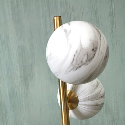 Gros plan sur un globe en verre effet marbre blanc du lampadaire Carrara et sa tige en métal doré