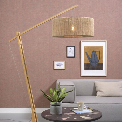 Lampadaire Iguazu en arceau, structure bambou naturel et abat-jour tressé jute, dans un salon à l'ambiance chaleureuse