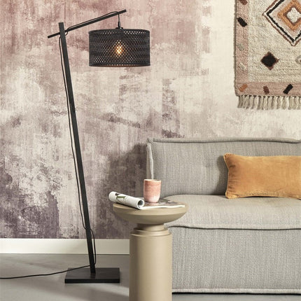 Lampadaire Java au pied noir incliné et abat-jour en bambou tressé noir, allumé près d'un canapé beige dans un salon