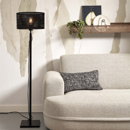 Lampadaire Java Droit en bambou noir allumé dans un salon chaleureux, près d'un canapé beige et d'une étagère