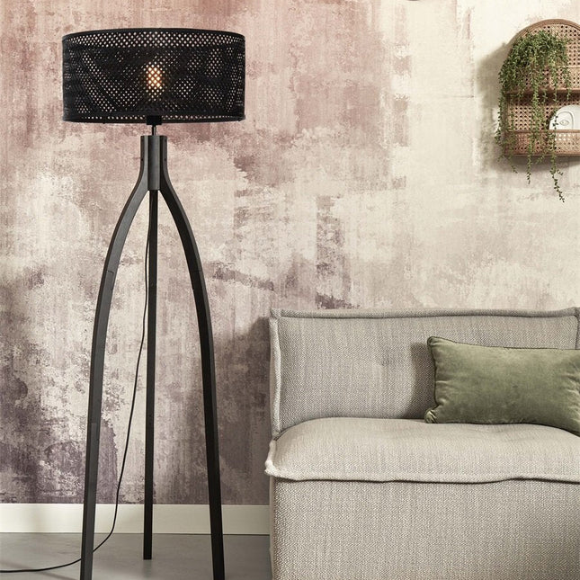 Lampadaire Java tripode en bambou noir avec abat-jour tressé, dans un salon aux tons rosés près d'un canapé