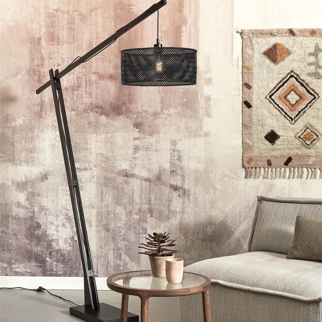 Lampadaire Java XL arqué en bambou noir avec abat-jour tressé au-dessus d'un canapé beige