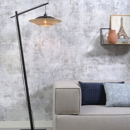 Lampadaire liseuse Kalimantan en bambou tressé noir et naturel, installé près d'un canapé dans un salon cocooning.