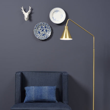 Lampadaire Lyon doré installé près d'un fauteuil bleu, mur foncé et assiettes décoratives