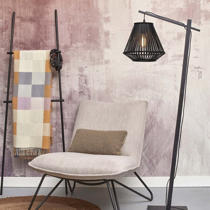 Lampadaire Merapi près d'un fauteuil beige, abat-jour en bambou noir diffusant une lumière chaude et graphique.