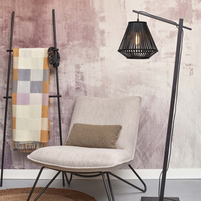 Lampadaire Merapi près d'un fauteuil beige, abat-jour en bambou noir diffusant une lumière chaude et graphique.