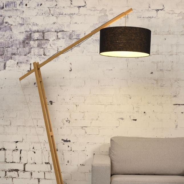 Lampadaire Montblanc en bambou naturel avec abat-jour en lin noir, dans un salon au mur brique blanchie