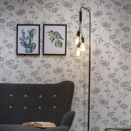 Lampadaire Oslo fer noir allumé devant un papier peint fleuri, ambiance chaleureuse de salon