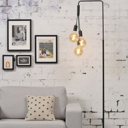 Lampadaire Oslo noir installé près d'un canapé gris devant un mur en briques blanchies