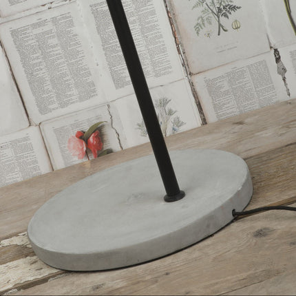 Base ovale en ciment brut du lampadaire Oslo, pied en fer noir posé sur une table en bois