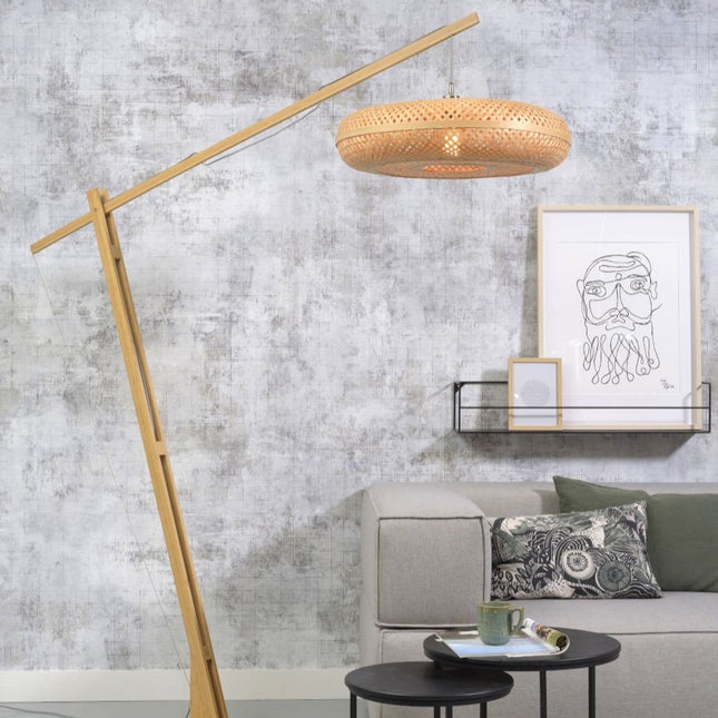 Lampadaire Palawan en bambou naturel au bras arqué, dans un salon avec canapé gris et étagère murale